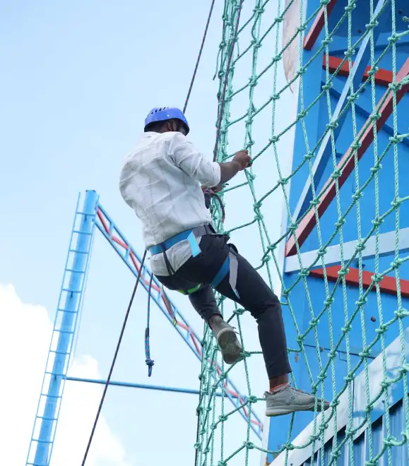 Participant climbing rope net obstacle in outdoor adventure zone